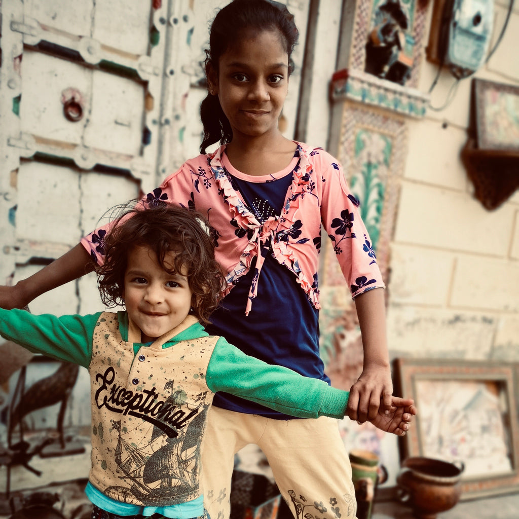 An older sister and little brother from a family of skilled artisans, posing for a photo in front of their home in Jaisalmere, India