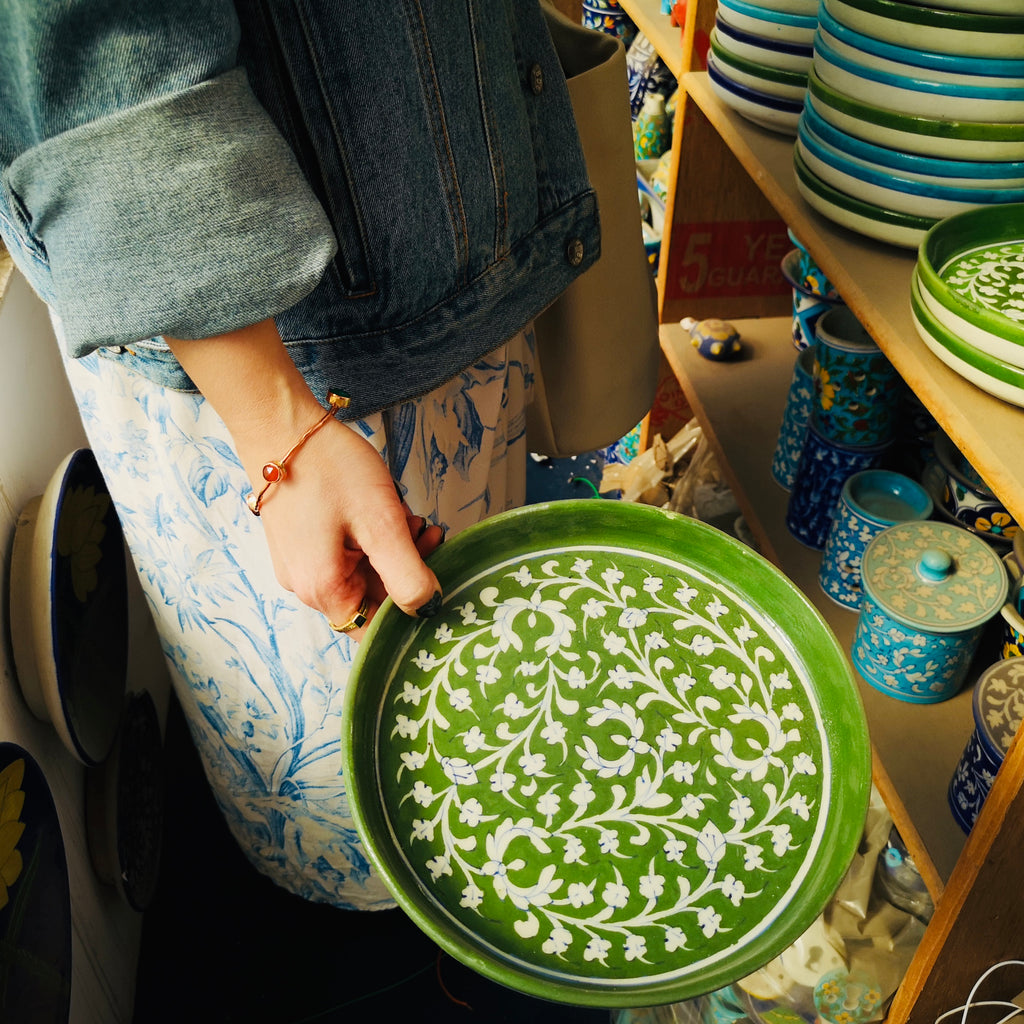 Founder of 43Collective holding a handmade green plate with white flowers from Jaipur Pottery